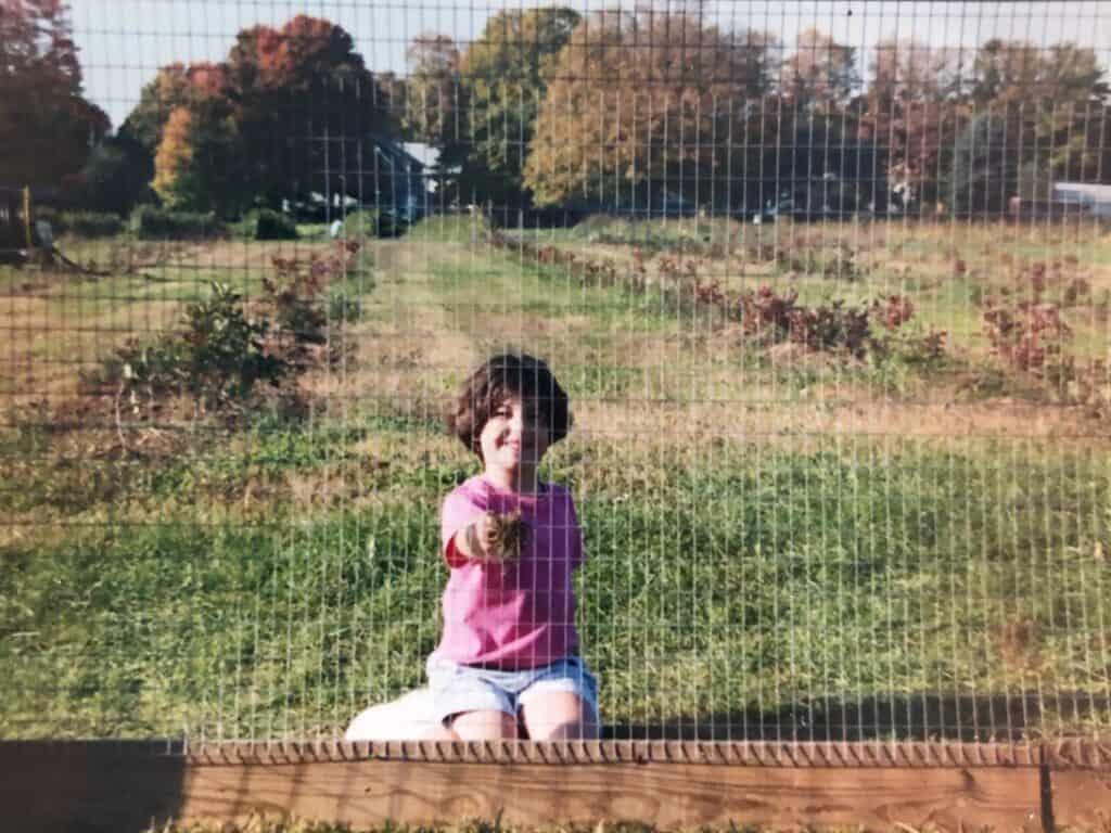 little girl holding a chicken in a corn field