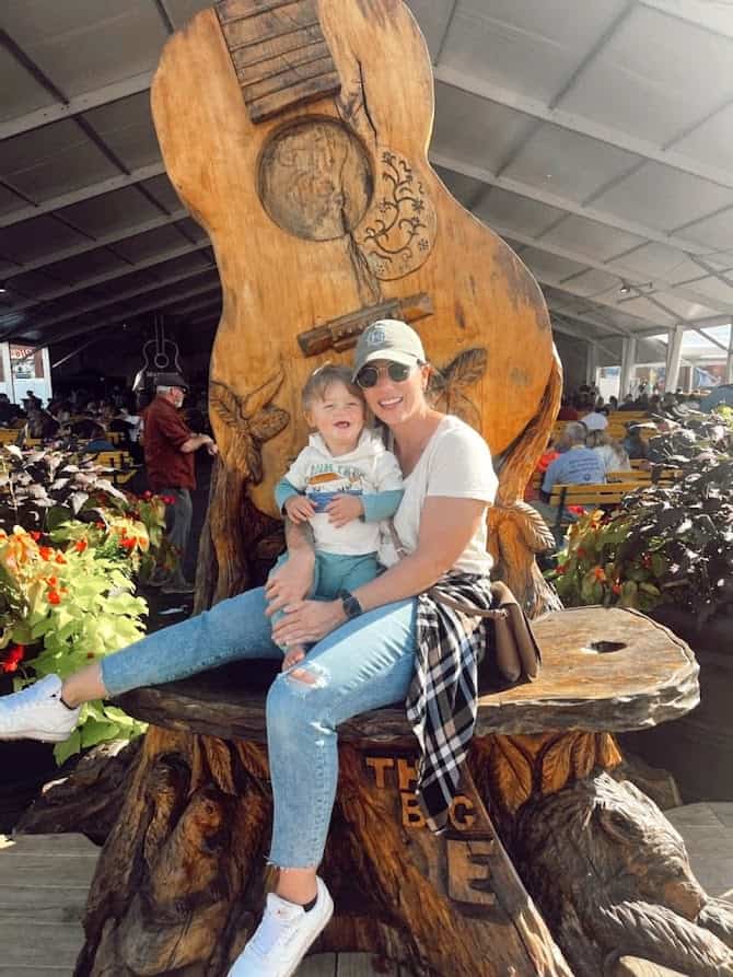 Girl posing with her son on a wooden guitar sculpture